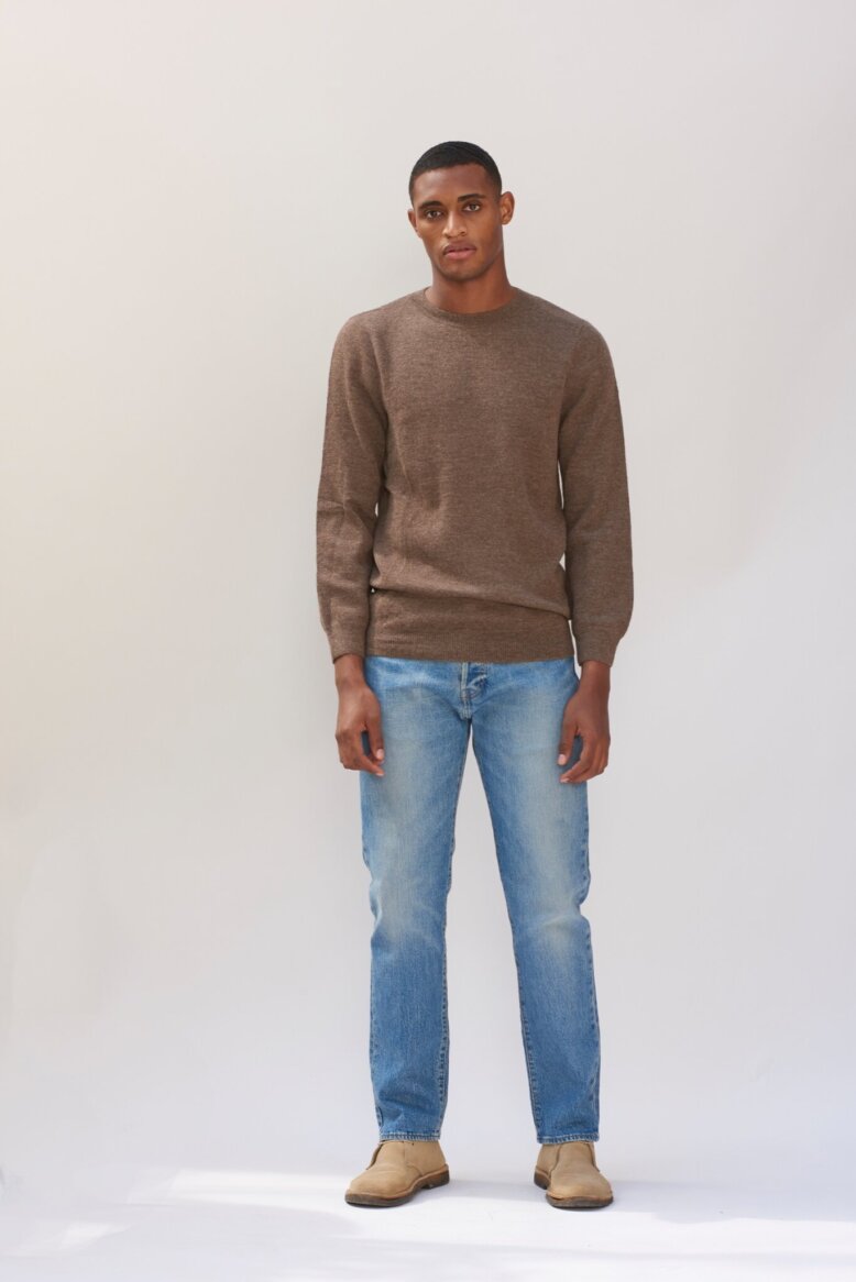 A brown, classic-fit, wool sweater set against a backdrop of textured, abstract sketches.