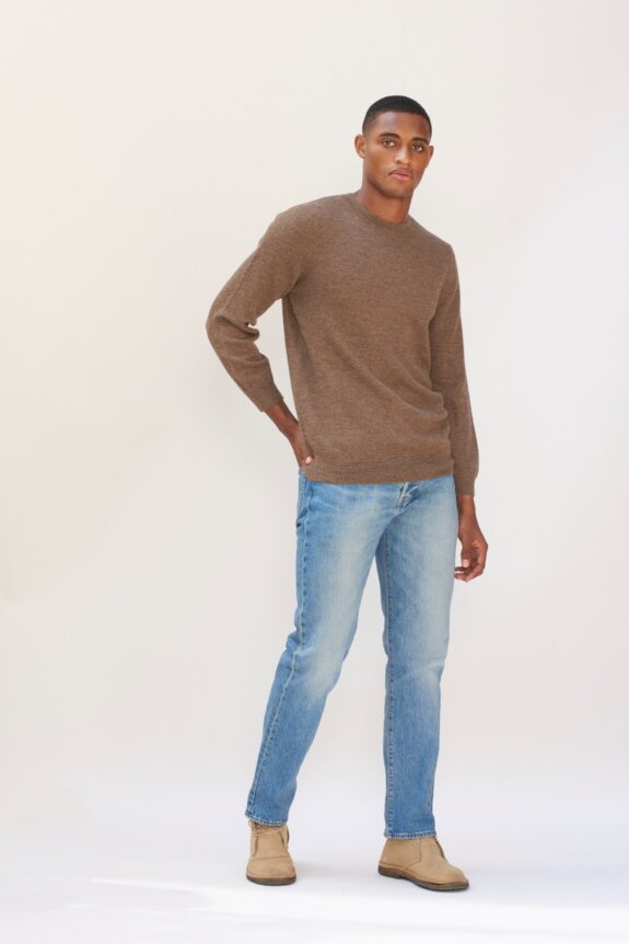 A charcoal gray, long-sleeve, crewneck sweater with ribbed cuffs and hem, displayed flat against a backdrop of vintage botanical and architectural sketches.