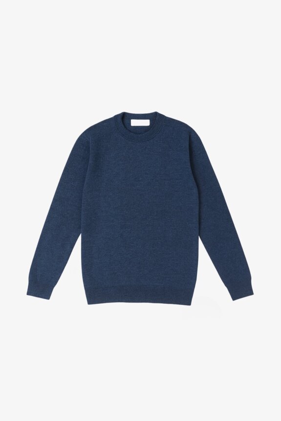 A navy blue, long-sleeved, crew-neck sweater with a classic fit, laid on a background of botanical illustrations.