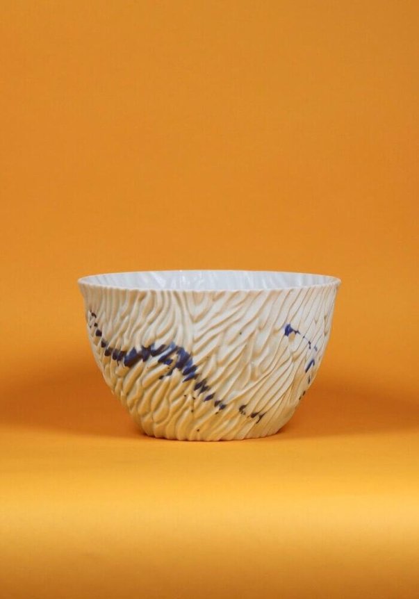 A textured ceramic bowl with a wavy surface and blue streaks, set against an orange background.