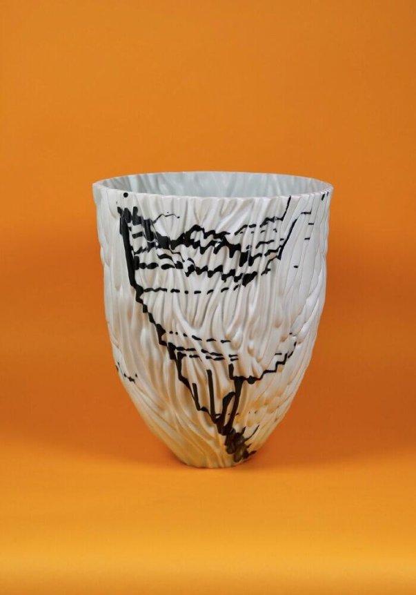 A textured white ceramic vase with black abstract patterns on an orange background.