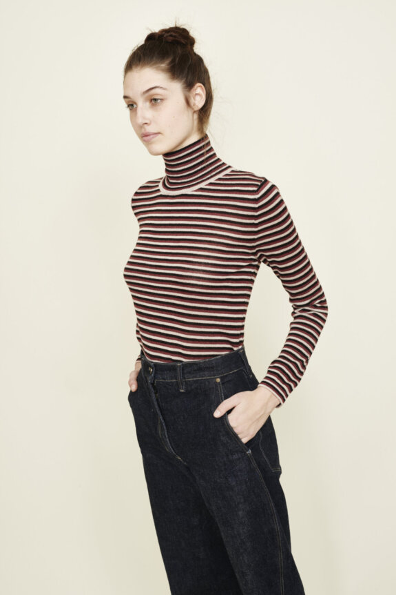 A person wearing a striped turtleneck and dark jeans, with their hair styled in a bun.