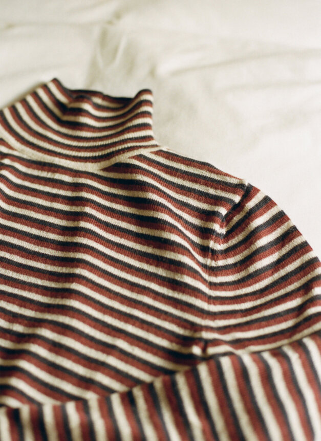 A striped turtleneck sweater with red, black, and beige stripes is laid on a light-colored surface.