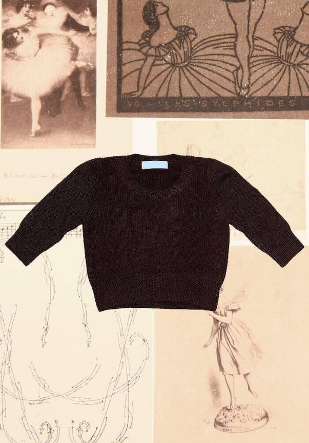 A black, fitted knit sweater with long sleeves is displayed against a background of vintage ballet-themed illustrations and photographs.