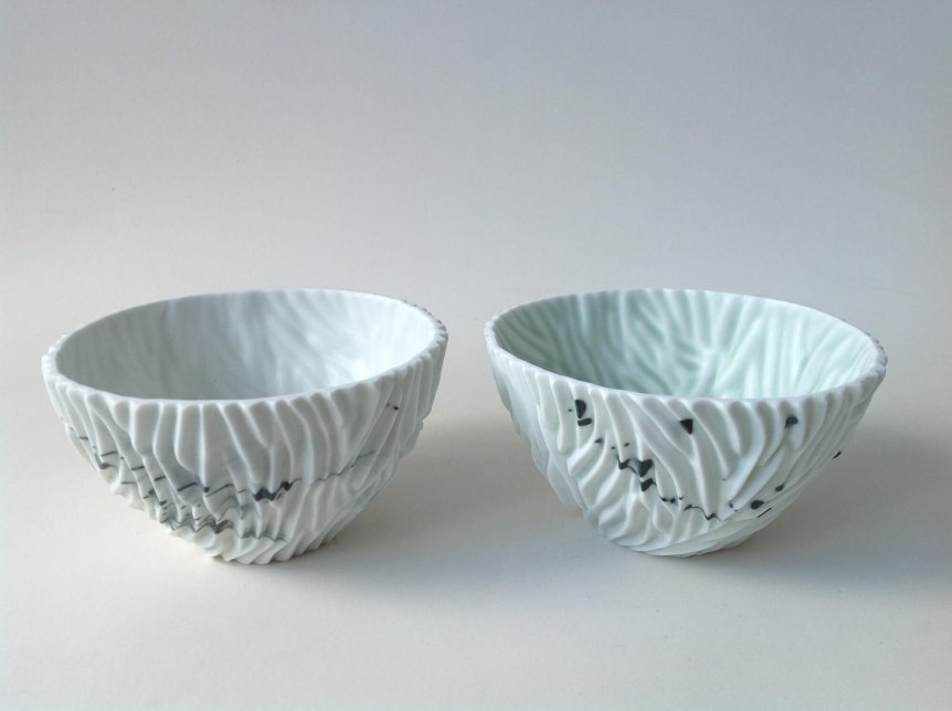 Two white ceramic bowls with textured surfaces and black line accents, placed against a plain background.