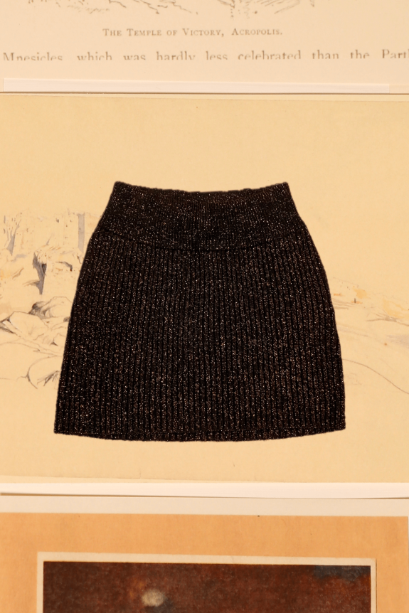 A black ribbed knit mini skirt with a metallic shimmer, displayed against a background featuring architectural illustrations.