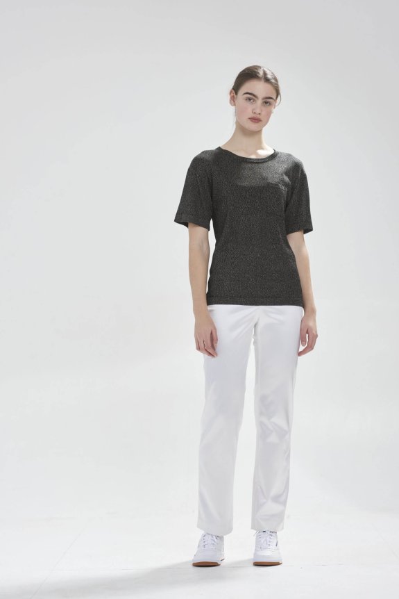 A model wearing a shimmering charcoal gray short-sleeve top with a straight fit, paired with tailored white pants and white sneakers.