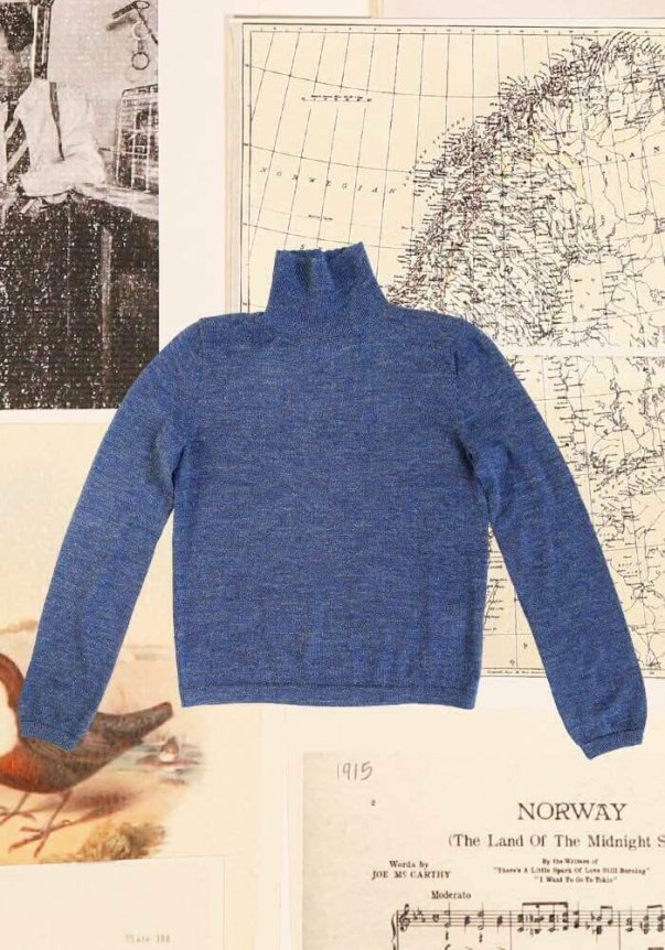 A blue, long-sleeve turtleneck sweater, finely knit, with a slim fit, laid against a backdrop of vintage maps and illustrations.