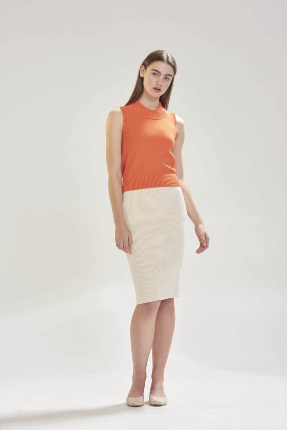 A model wears a fitted, sleeveless orange knit top paired with a high-waisted, cream pencil skirt, crafted from ribbed fabric, exuding a sleek and sophisticated look.