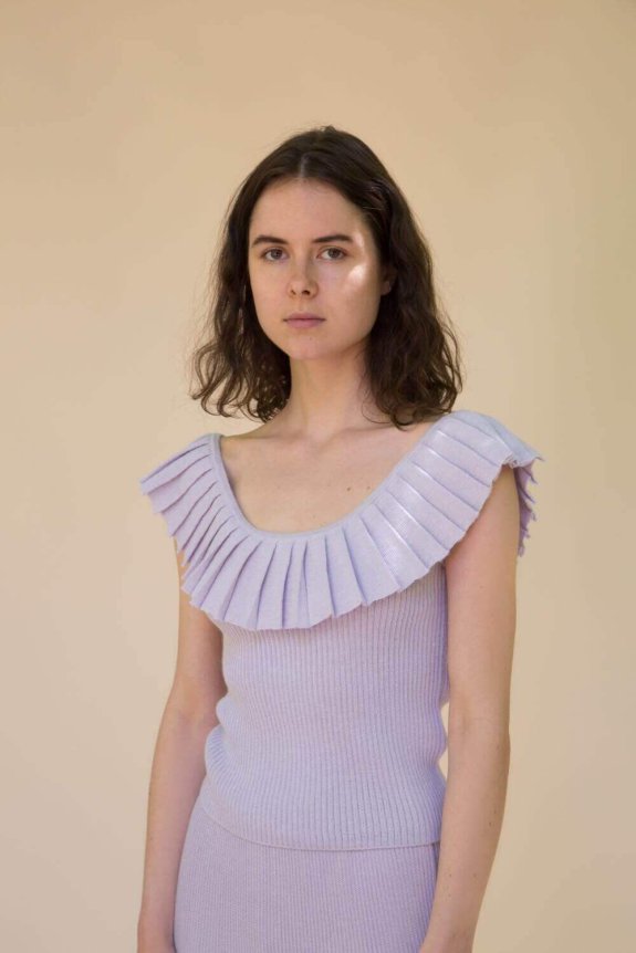 A model wearing a lilac ribbed knit dress with a fitted silhouette and distinctive pleated ruffle detailing on the neckline.