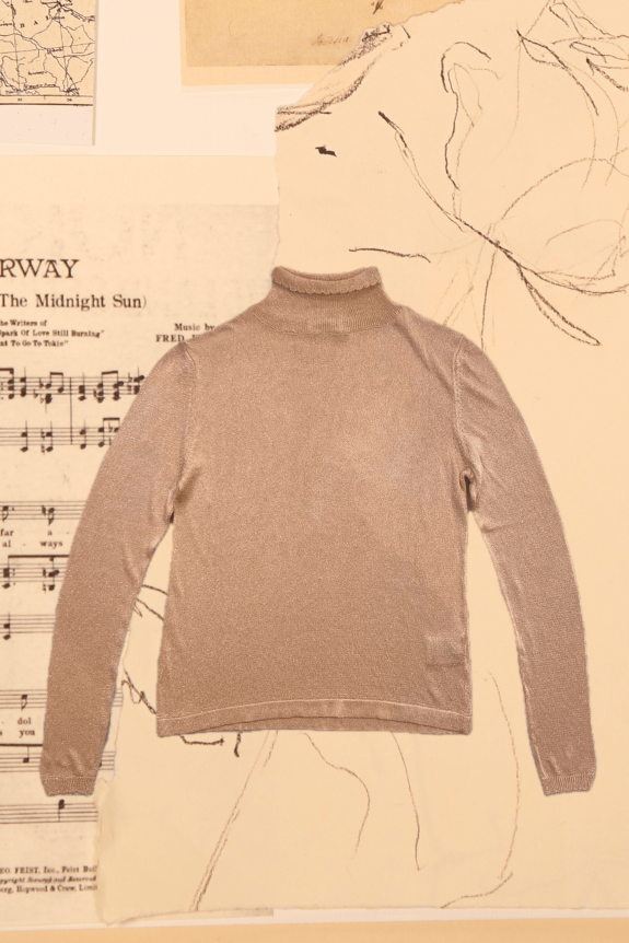 A beige, long-sleeve, fitted turtleneck sweater made from a shimmering, lightweight knit material, placed on a background of vintage sheet music and abstract sketches.