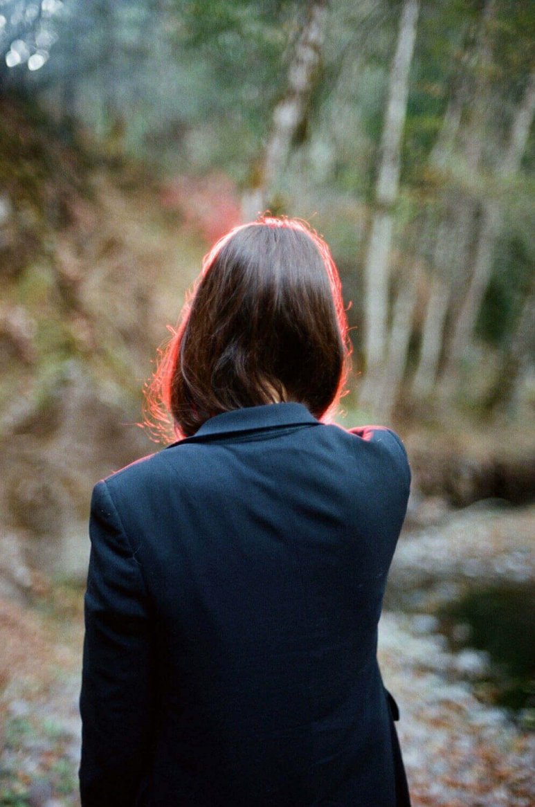A person wearing a navy blazer with a tailored fit, standing in a natural, wooded setting.