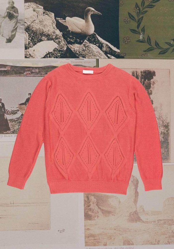 Coral pink knit sweater with diamond-shaped openwork pattern, featuring ribbed cuffs and hem, laid on a vintage photo collage background.