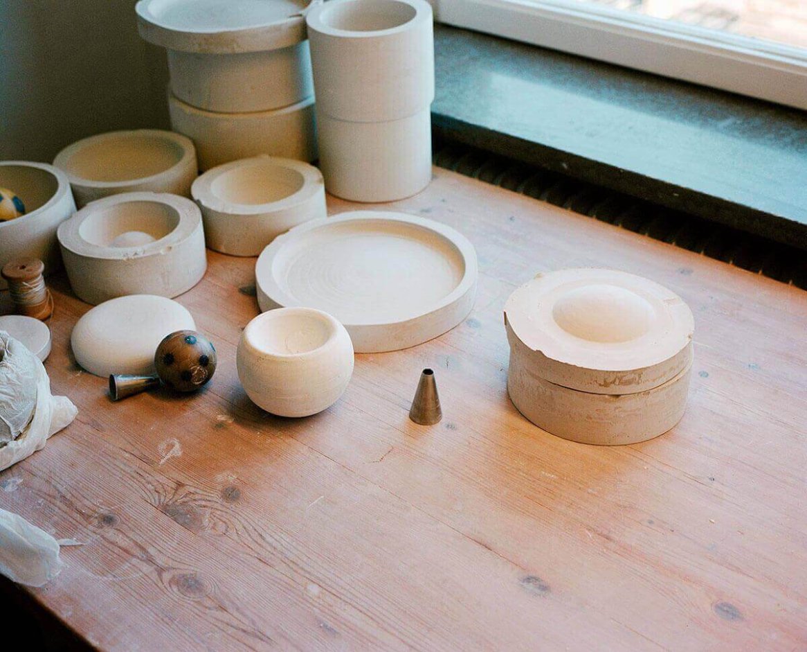 Various plaster molds and tools are scattered on a wooden table near a window.