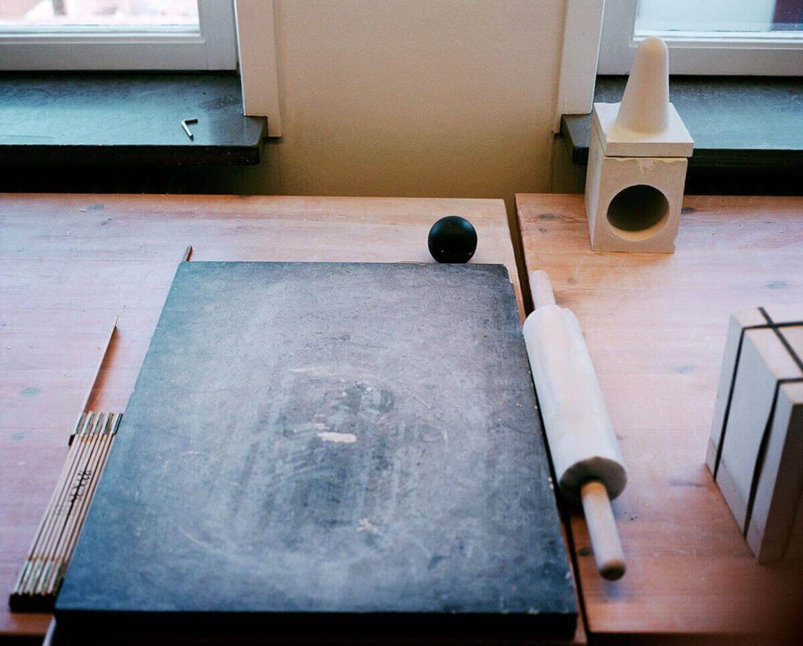A wooden table with a rolling pin, a slate board, a black ball, and geometric shapes arranged by two windows.