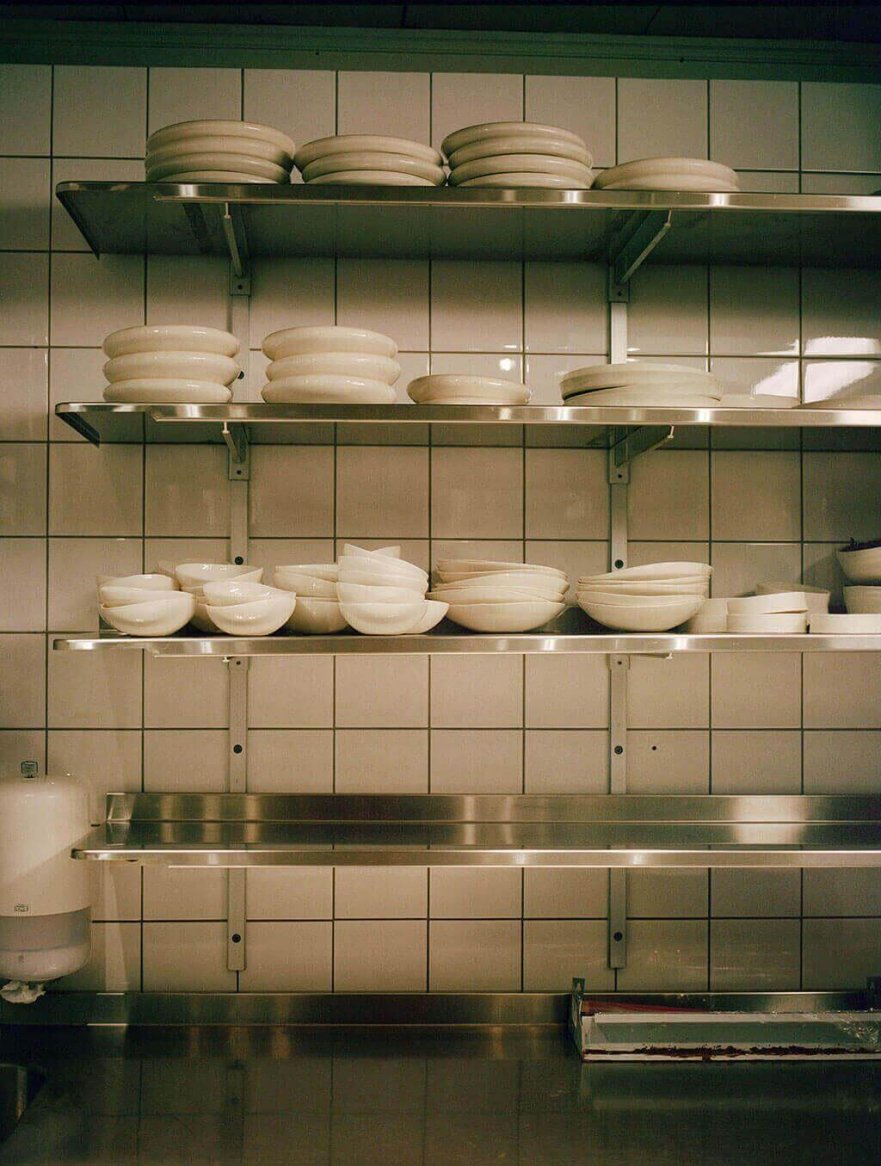 Shelves stacked with white ceramic dishes against a tiled kitchen wall.