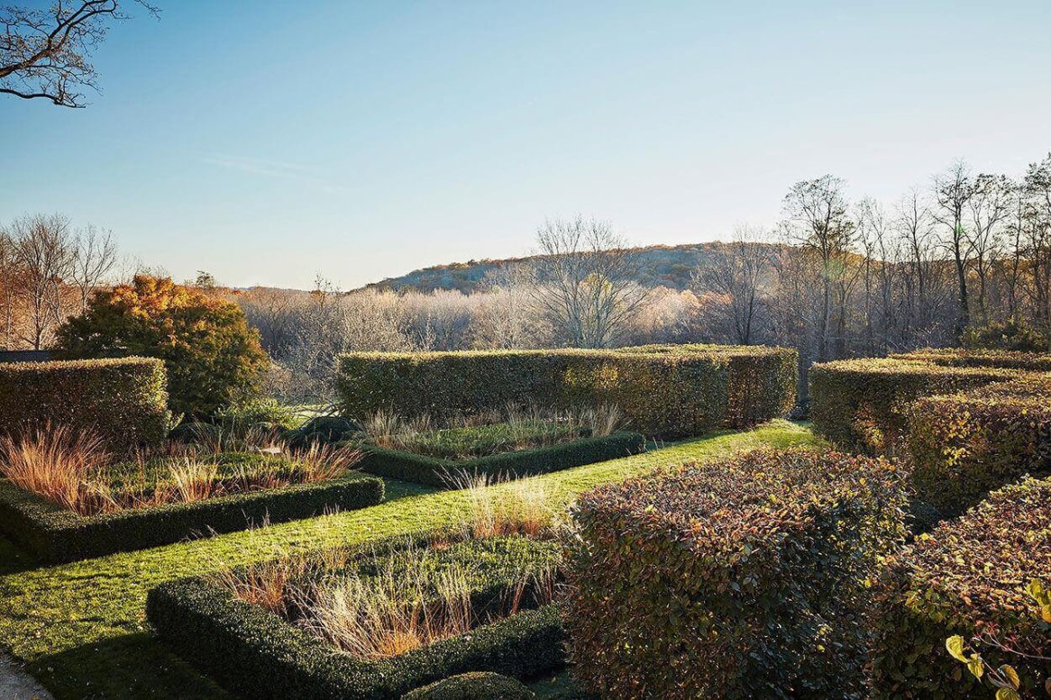 A scenic garden with neatly trimmed hedges and patches of ornamental grasses under a clear blue sky.