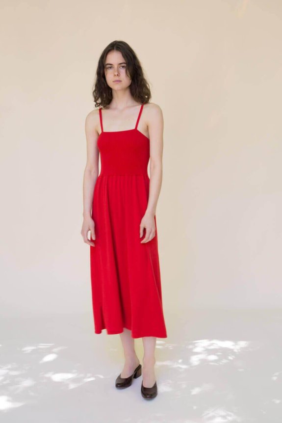A red sleeveless midi dress with spaghetti straps, featuring a fitted bodice and flowing skirt, made of a lightweight, textured material.