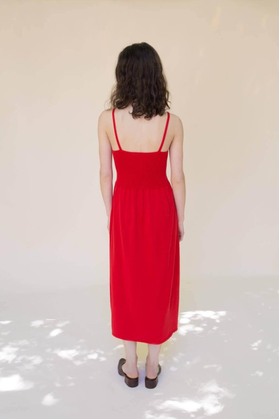 A back view of a red sleeveless dress featuring a ribbed bodice, fitted waist, and thin straps, made from a knit material.