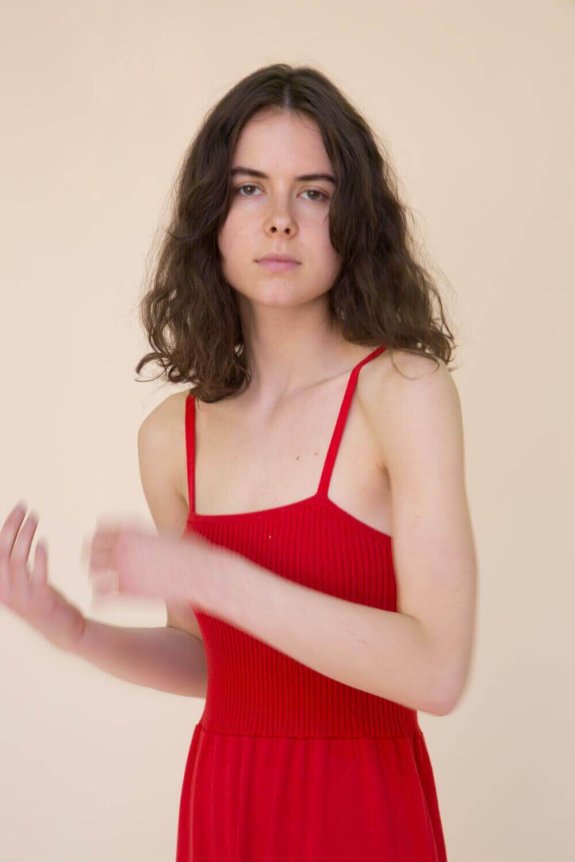 A woman in a red, ribbed, sleeveless dress with thin straps and a fitted bodice, made of a lightweight fabric.