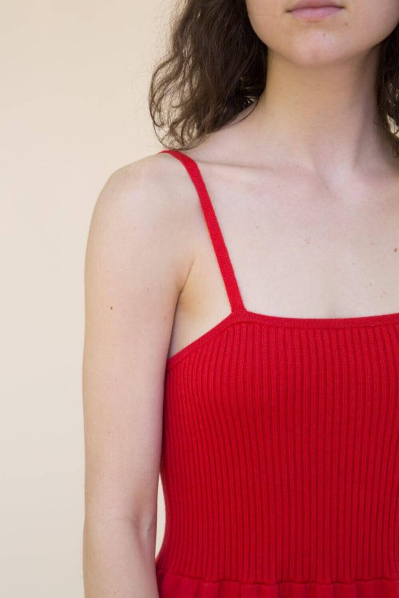 A woman is wearing a red, ribbed-knit, sleeveless dress with spaghetti straps, featuring a fitted waist and flowing skirt.