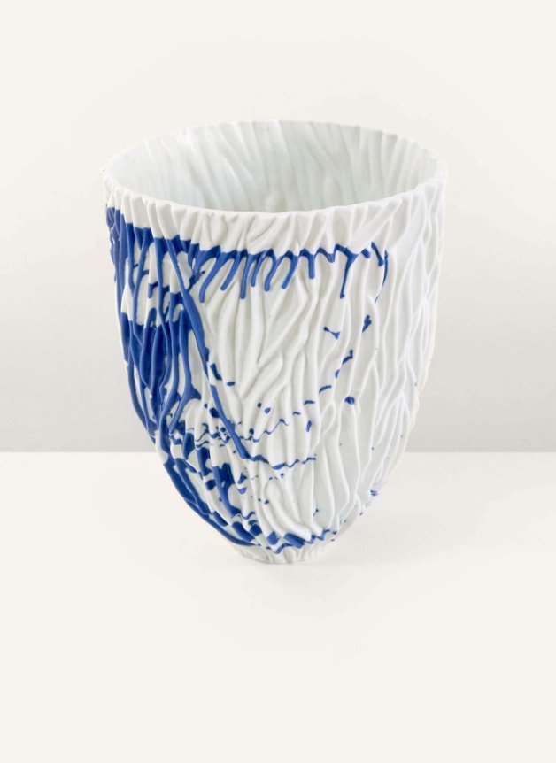 A textured white ceramic vase with blue splatter design on a plain background.