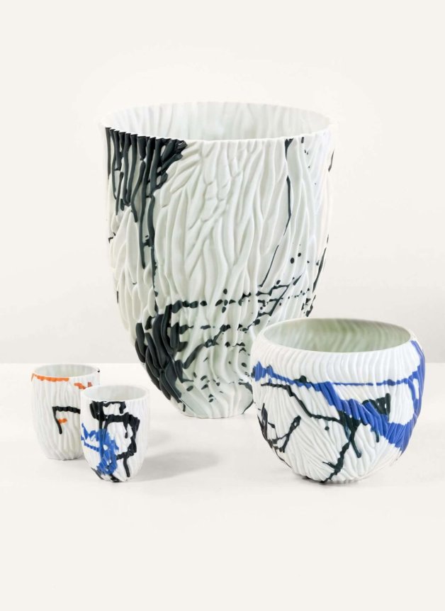 A set of textured white ceramic vases and cups with abstract black, blue, and orange splatter designs.