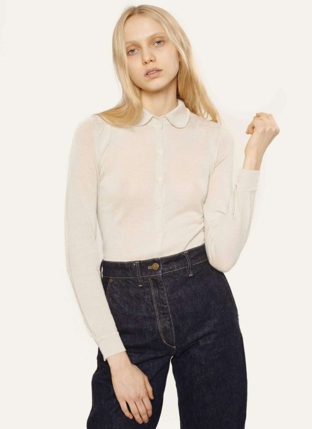The image shows a model wearing a cream long-sleeve collared shirt made of lightweight material, paired with high-waisted dark denim jeans.