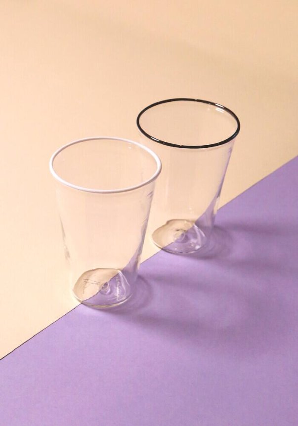 Two clear plastic cups with black and white rims placed on a beige and pastel purple surface.