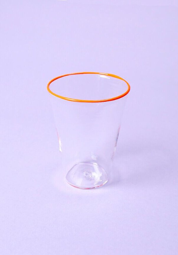A clear glass with an orange rim on a light purple background.
