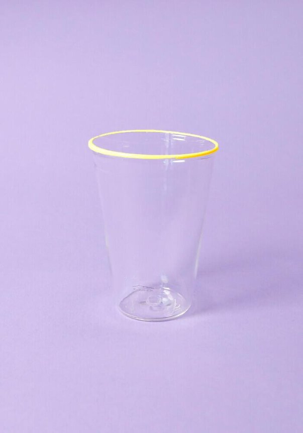 A transparent glass with a yellow rim against a light purple background.