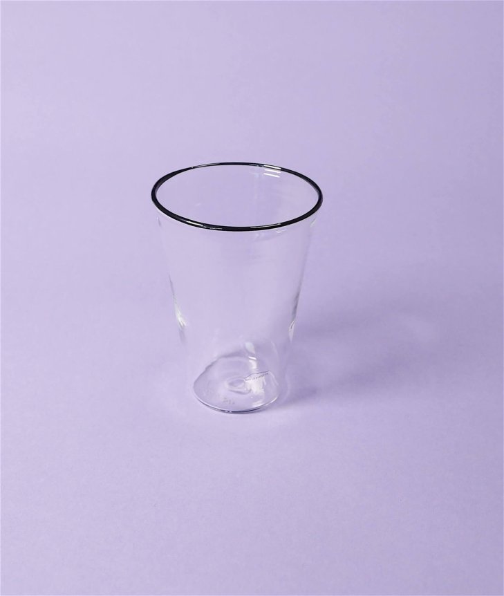 A clear, transparent glass with a black-rimmed edge, set against a pastel purple background.