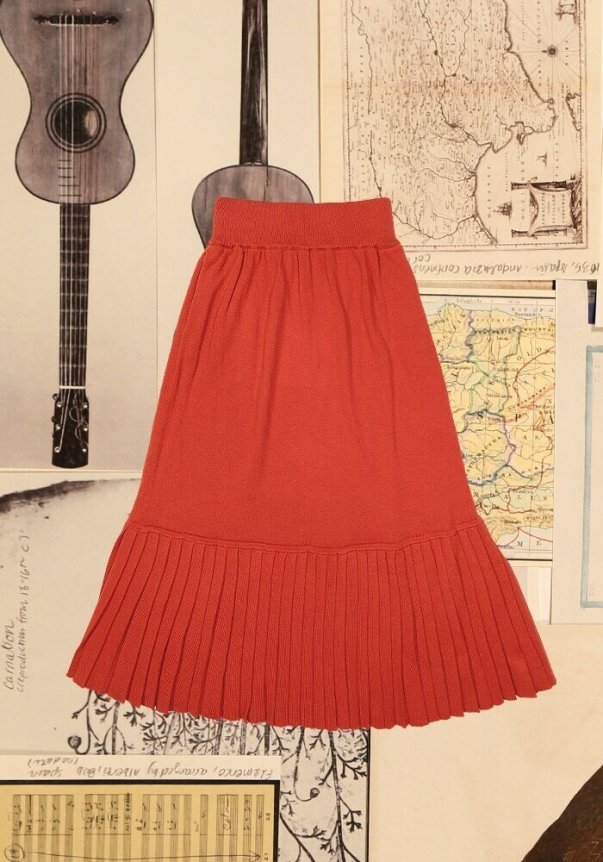 A rust-colored, pleated midi skirt with an elastic waistband, laid on vintage-style maps and sheet music background.