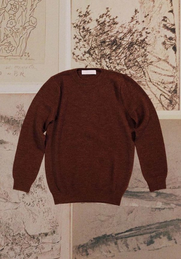 A rose-colored, classic crew neck sweater with ribbed cuffs and hem, laid on a floral and sketch background.