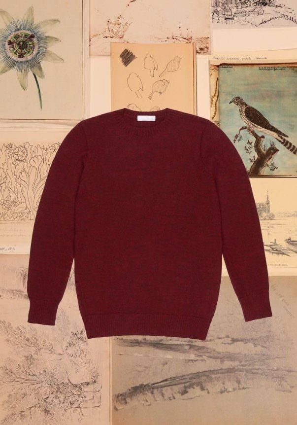 A brown, wool-blend knit sweater with a classic crew neck style, set against a backdrop of artistic sketches.