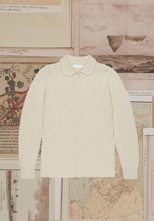 A cream-colored, long-sleeve button-up blouse with a peter pan collar and ruched shoulders, set against a background of vintage maps.