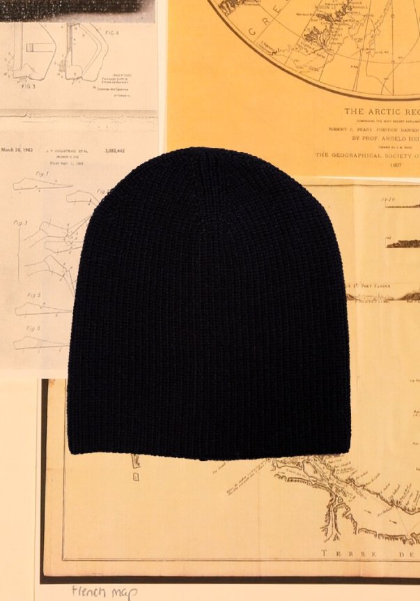 A cream-colored, cable-knit sweater with a relaxed fit, displayed against a collage of vintage black and white photographs and illustrations.