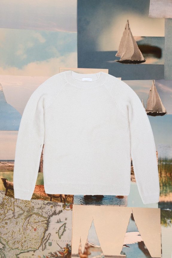 A cream-colored, textured knit crewneck sweater with a regular fit, displayed against a collage backdrop featuring sailboats and maps.