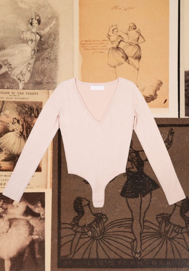 A light pink, long-sleeved V-neck bodysuit is displayed over vintage ballet-themed illustrations, highlighting a classic and elegant fit.