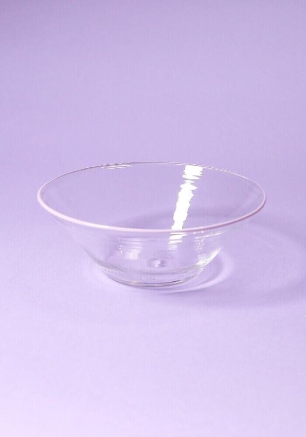 A clear glass bowl on a pastel purple background, reflecting light.