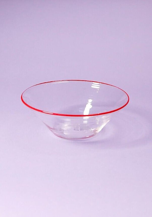 A clear glass bowl with a distinctive red rim, set against a soft purple background.