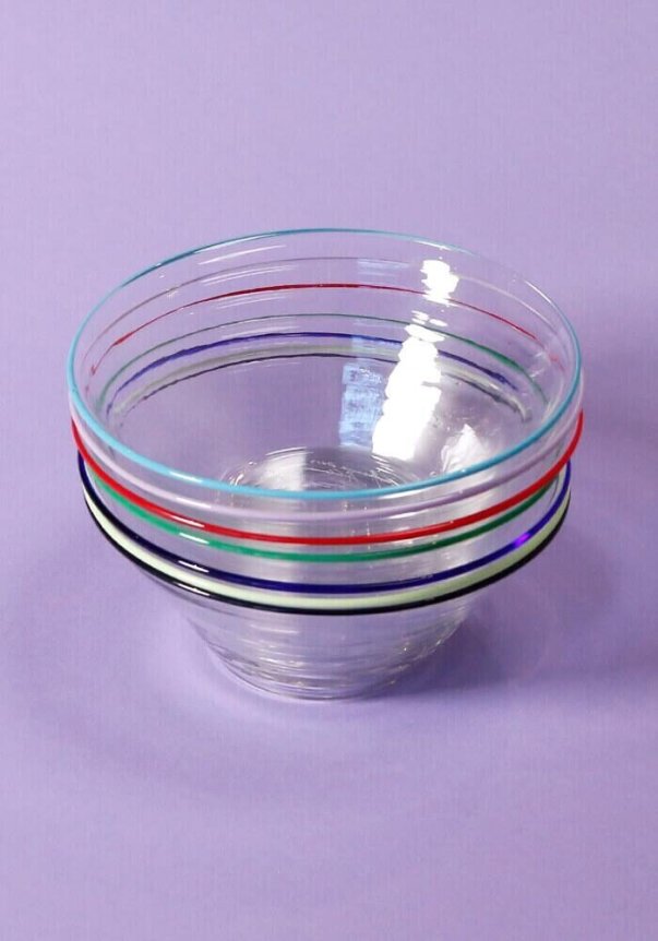 A set of clear glass bowls with colorful rim stripes, placed on a light purple surface.