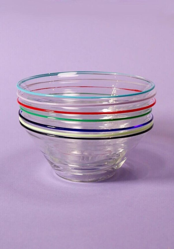 A stack of clear glass bowls with colorful rim accents on a purple background.