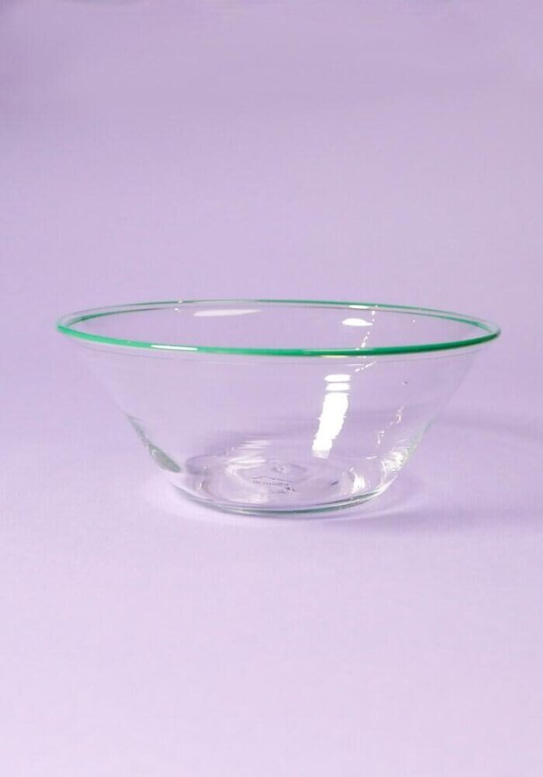 A transparent glass bowl with a green rim, set against a light purple background.