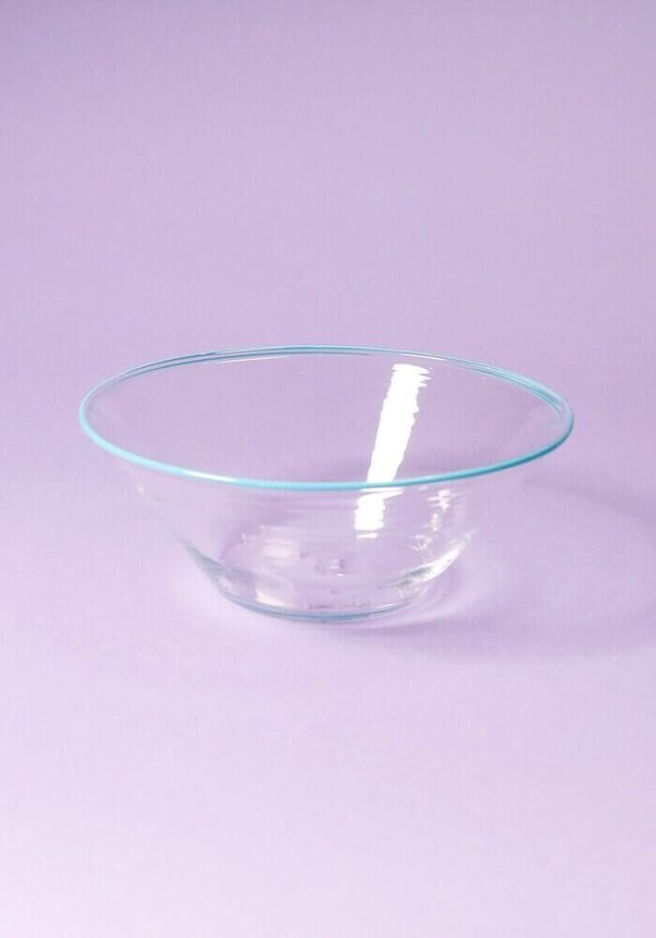 A clear glass bowl on a pastel purple background.