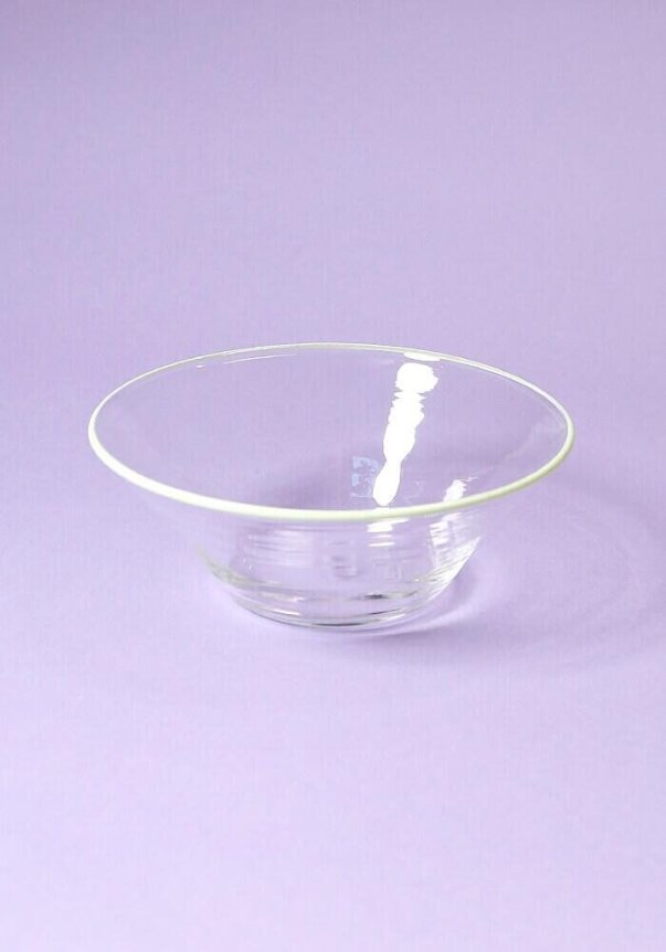 A transparent glass bowl with a subtle reflective sheen is set against a light purple background.