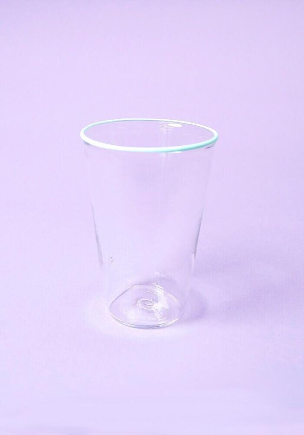 A clear glass cup with a minimalistic design on a pastel purple background.