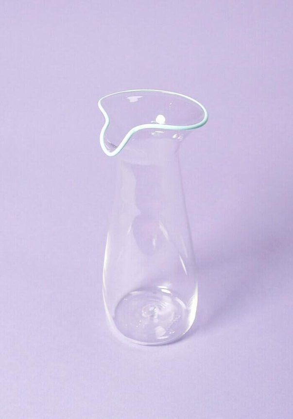 A clear glass pitcher with a uniquely shaped, wavy rim on a purple background.