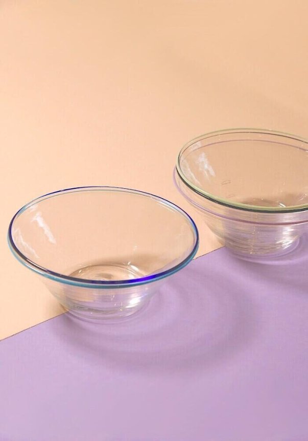 Two clear glass bowls are placed on a peach and lavender colored background.