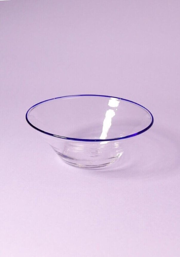 A clear glass bowl with a blue rim on a light purple background.